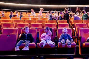 3 Kinderen die in theater stoelen zitten en naar het theater wijzen, tijdens de cultuureducatie