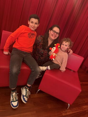 Mama Vassia, zoon James en dochter Lily zitten op stoeltjes in het theatercafé van Theater Heerlen.
