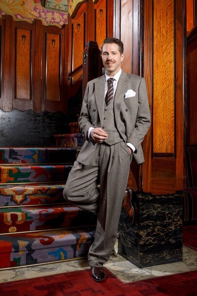 William Spaaij poseert in grijs pak in een art deco foyer.