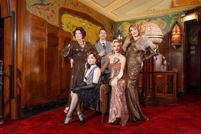 De vijf hoofdrolspelers poseren in een art deco stijllobby in typische jaren dertig stijl avondkleding.