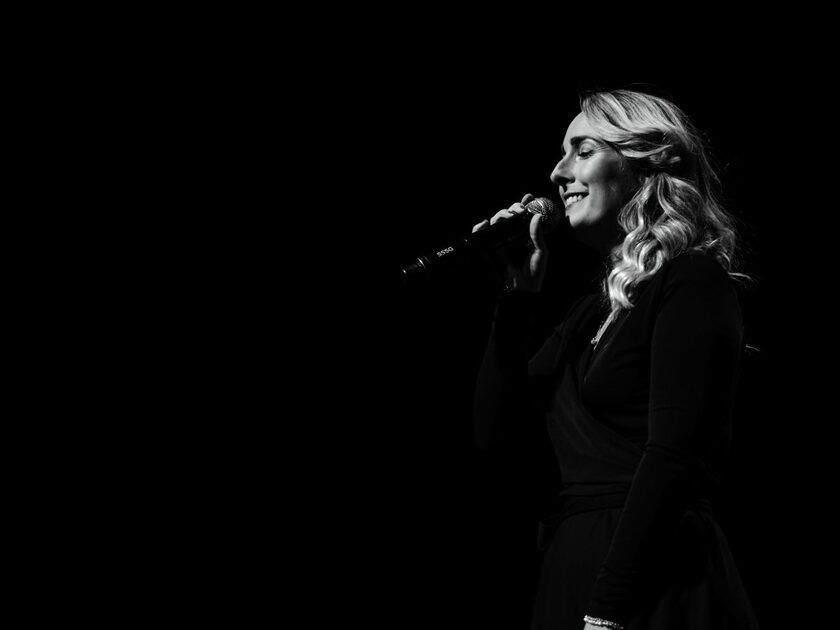 Celine Weerts zingt op het podium in een microfoon.