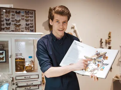 Bioloog Mátyás Bittenbinder wijst naar een afbeelding in een open boek.